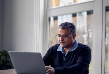 side view of a man sitting at the kitchen table with his laptop and paperwork